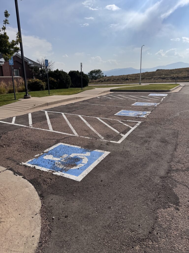 Faded handicap parking stalls and worn, cracked asphalt before sealcoating and restriping