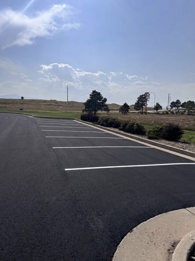 Fresh black sealcoat and new white parking stall lines along a landscaped curb