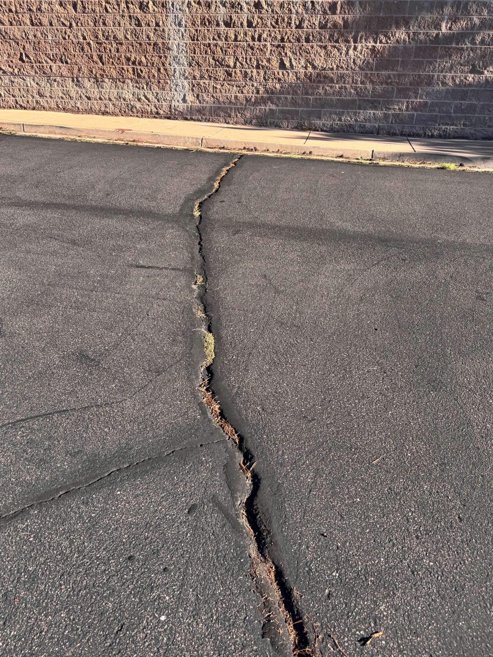 Long asphalt crack running to the curb in a commercial parking lot