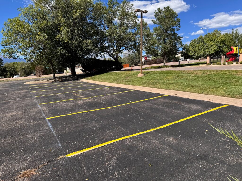Fresh yellow parking stall lines along a curb in a commercial parking lot
